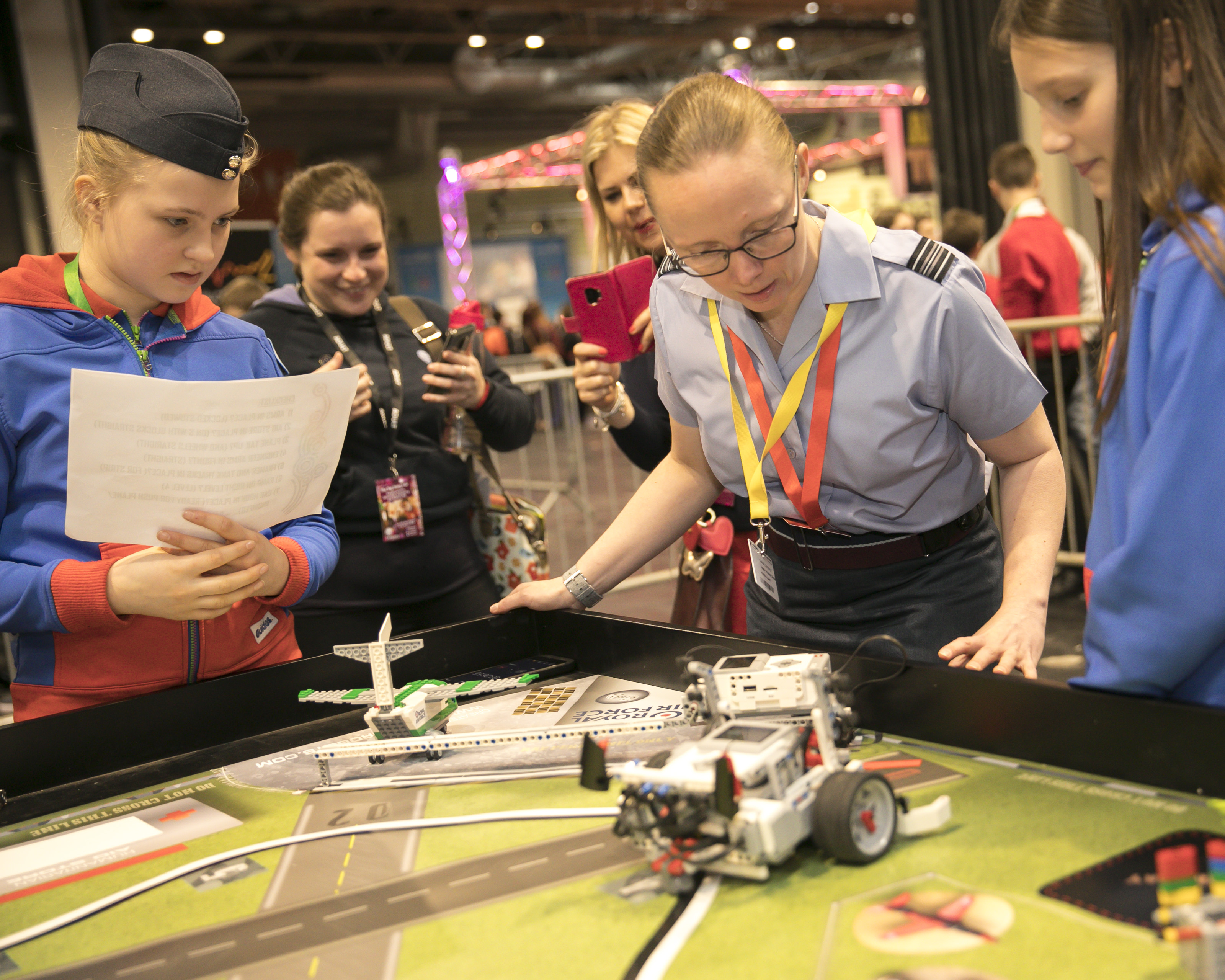 Image shows RAF STEM ambassador and school children looking at table with miniature model airfield on top. 
